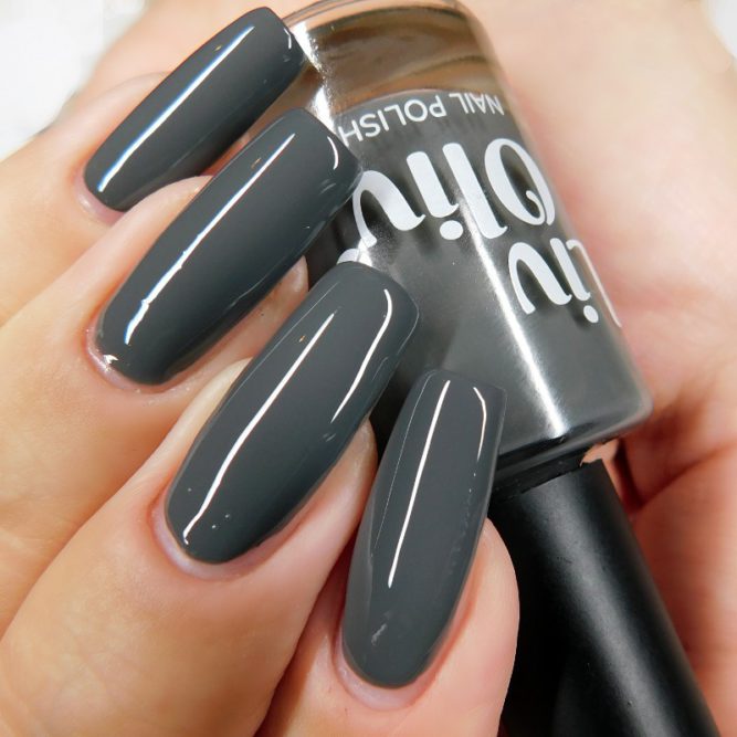 Close up of nails painted charcoal grey holding LivOliv 'Charlotte' nail polish bottle